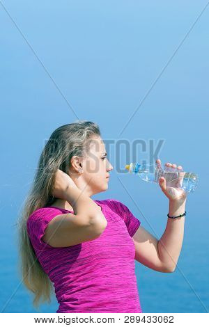 Side View Of Beautiful Girl In Sport Clothes Drinking Water After Workout On The Beach. Young Woman 