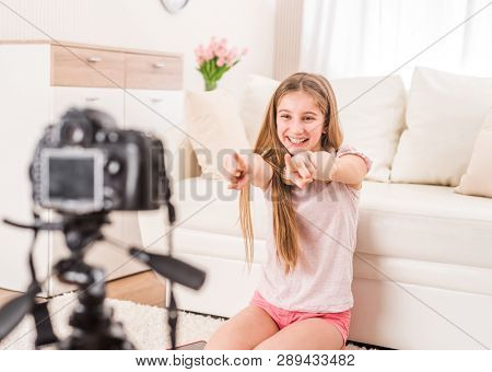 Young smiling videobloger teen girl is pointing at camera in living room