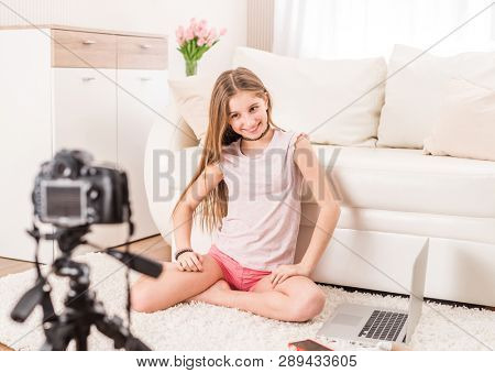 Young smiling videobloger teen girl is pointing at camera in living room