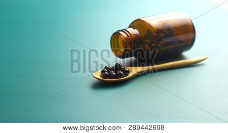 Black Bolus On Wooden Spoon And Bottle On Green Background