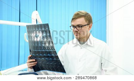 Male Doctor Radiologist Looking At X-ray, Touching His Glasses In Medical Cabinet, Medicine Concept.