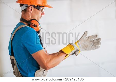 Caucasian Worker In Hard Hat And Safety Glasses Wearing Safety Gloves And Preparing For Work. Constr