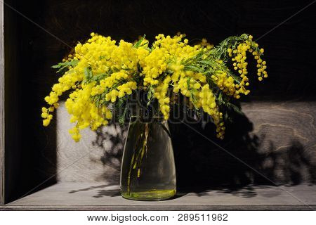 A Branch Of Yellow Flowers Of Mimosa In A Glass Vase On A Black Background.