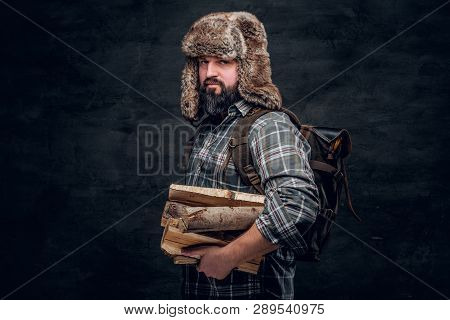 Portrait Of A Bearded Woodcutter With A Backpack Dressed In A Plaid Shirt And Trapper Hat Holding Fi