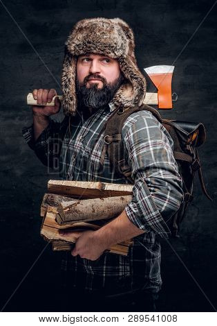 Portrait Of A Bearded Woodcutter With A Backpack Dressed In A Plaid Shirt And Trapper Hat Holding Fi