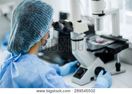 The Doctor Is Looking Through A Microscope With A Scientific And Medical Topic. A Scientist And A La
