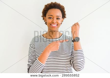 Young beautiful african american woman wearing stripes sweater over white background In hurry pointing to watch time, impatience, upset and angry for deadline delay