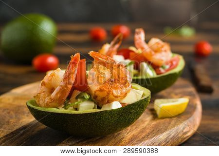 Halves Of Avocado Filled With Salad From Shrimps, Cherry Tomatoes, Feta Cheese And Arugula On Wooden