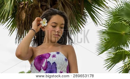 Young Girl With Floral Sundress Smiling With Flower In Hair Standing Under Palm Tree