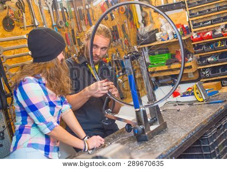 Handsome Beraded Guy And The Pretty Girl Repairing Bicycle In The Workshop Together