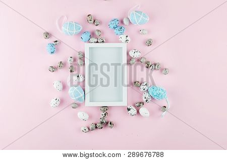 White Empty Frame With  Decoration Colored Eggs And Sweet Easter Candy Around On Light Pink Backgrou