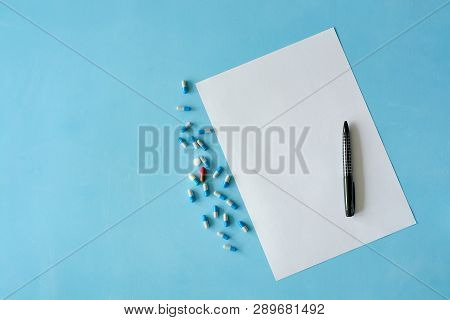 White Sheet Paper With Black Pen And Colored Different Pills, Capsules On Blue Background With Copy 