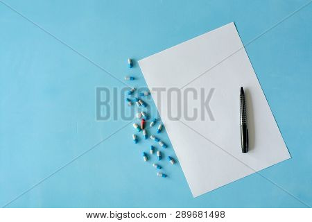 White Sheet Paper With Black Pen And Colored Different Pills, Capsules On Blue Background With Copy 