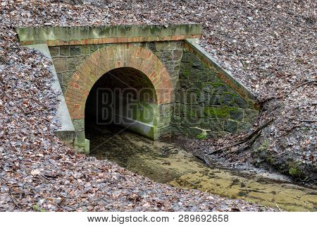 Stone Culvert Over The Road For A Small River. A Small Stream In A Forest Area. Season Of The Spring