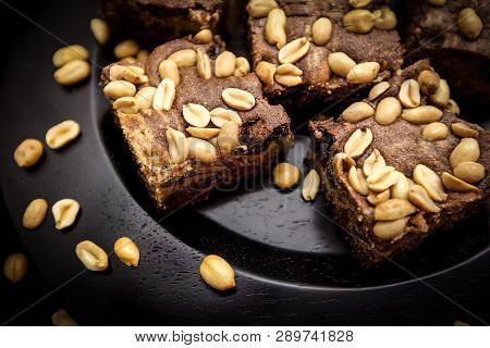 Homemade Brownies With Peanuts On A Dark Brown Plade