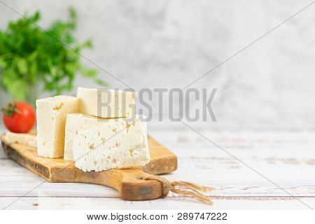Large Pieces Of Feta Cheese On Old Wooden Cutting Board And Cherry Tomatoes On Light Background. Sel