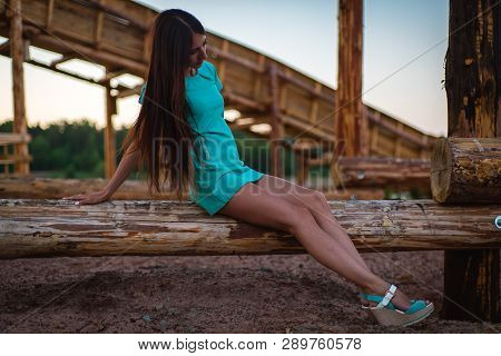 Girl In Turquoise Short Dress Sitting On A Tree Log