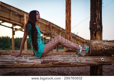 Girl In Turquoise Short Dress Sitting On A Tree Log