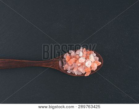 Himalayan Pink Salt In Spoon On Black Stone Background. Copy Space