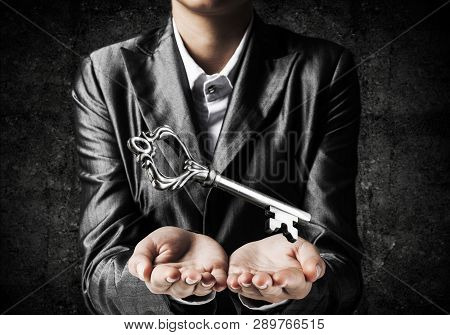Cropped Image Of Businessman In Suit Keeping Big Key In Hands With Dark Wall On Background.