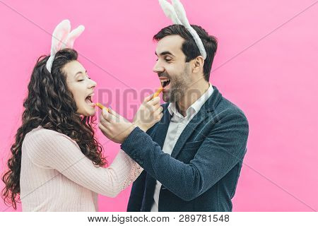 Young Happy Couple Standing On Pink Background. On The Head Of The Ears Of The Bunny. During This Ma