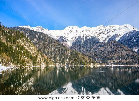 Beautiful Mountain Lake In The Spring. In The Background, Mountains Covered With Snow Are Reflected 