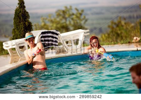 Young people spraying each other with water guns in swimming pool in nature