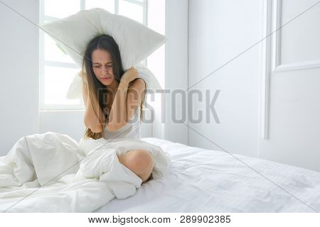 Young caucasian woman covering her head and ears with pillows.