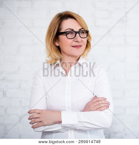 Portrait Of Mature Business Woman In Eyeglasses Posing Over White Brick Wall