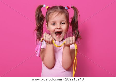 Laughing Cute Girl Wears Rose T Hirt, Stands Isolated Over Pink Background, Hold Bright Skipping Rop