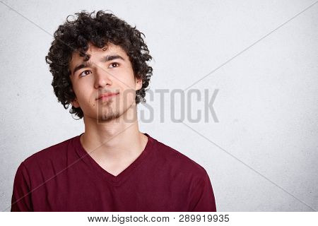Portrait Of Thinking Young Man With Dark Curly Hair, Stands With Thoughtful Facial Expression, Dress