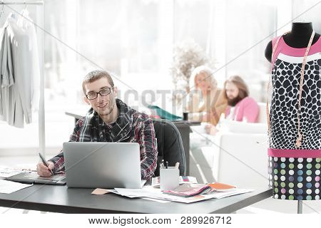 Designer Using Laptop And Graphics Tablet To Create Sketches Of New Clothes