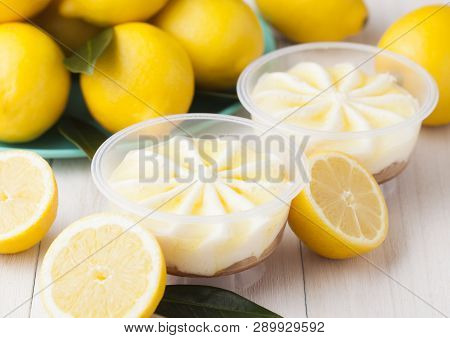 Plastic Jar With Lemon Cheesecake Mousse Dessert With Raw Lemons On Light Wooden Background