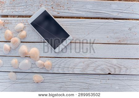 The Smartphone Lies In The Encircling Of Seashells On Wooden Boards.
