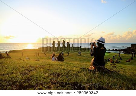 Female Tourist Taking Photos Of The Famous Sunset Scene At Ahu Tahai, Archaeological Site On Easter 