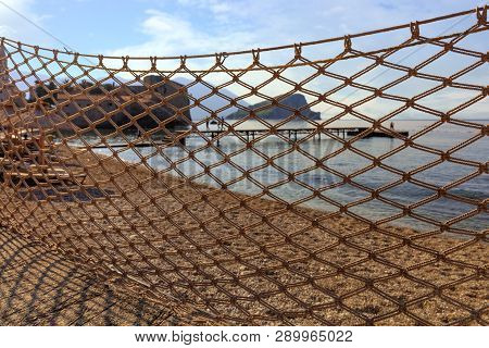 Through Pattern Of Large Cells Of The Fishing Net, Drying In The Sun, A Pier, An Old Castle And The 