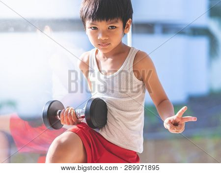 Little Boy Is Working Out With Dumbbell By The Windows City.