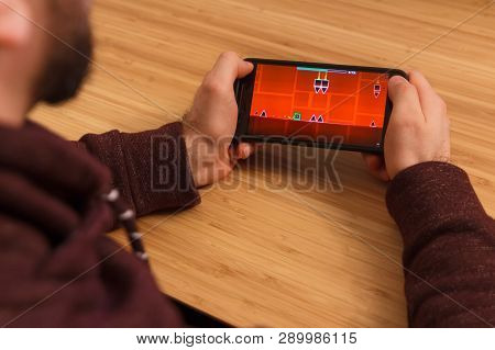 Prague, Czech Republic - March 16, 2019: Man Holding A Smartphone And Playng The Geometry Dash Mobil