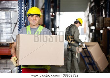 ภาพของความสุขกลางจ้างผู้ใหญ่ด้วยกล่องกระดาษแข็งและเพื่อนร่วมงานกด handtruck ที่คลังสินค้า