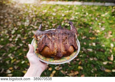 A Man Is Holding A Dish Of Fried Chicken. Grilled Whole Chicken On The Background Of The Garden, Clo