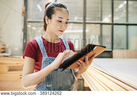 Serious Young Vietnamese Carpentry Shop Manager Checking E-mails And Orders From Clients On Tablet C