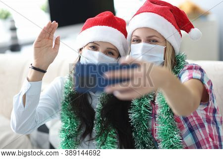 Two Women Friends In Protective Face Masks And Red Santa Hats Are Photographed On Phone Portrait. Me