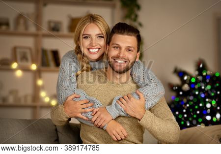 Loving Young Man And Woman Posing At Home On Xmas Eve, Sitting On Floor My Couch In Living Room, Emb
