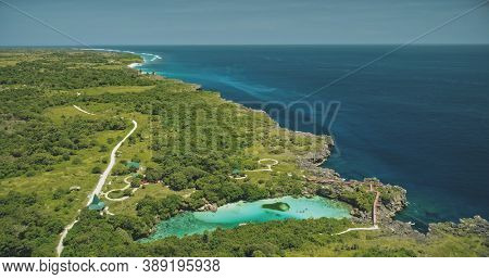 Aerial view of turquoise salt water lake at green tropic trees. Buildings and road at greenery valley of Sumba island, Indonesia. Amazing Asia seascape of sea bay admist rock coast at drone shot