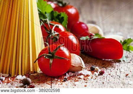 Italian Dry Pasta Spaghetti With Tomatoes And Fresh Herbs On A Dark Wooden Background, Selective Foc