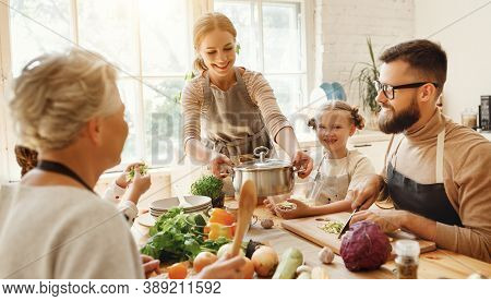 Positive Young Housewife With Little Daughters, Husband And Grandmother Gathering Around Kitchen Tab