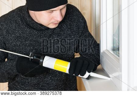 Side View Of A Man In Repair Clothes Sealing The Slots Of Plastic Windows Using White Selicon And A