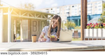 Woman With Headphones Writes In Notebook, With Laptop Outside In Park. Happy And Smiling Girl Workin
