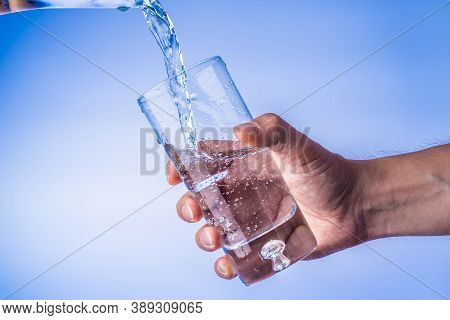 Filling Up The Glass With Water, Hand Holding Glass Against Bright Blue Background