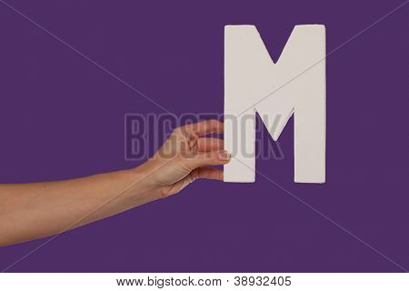Femelle main tenant jusqu'à la capitale majuscule M isolé contre une vue fond violet